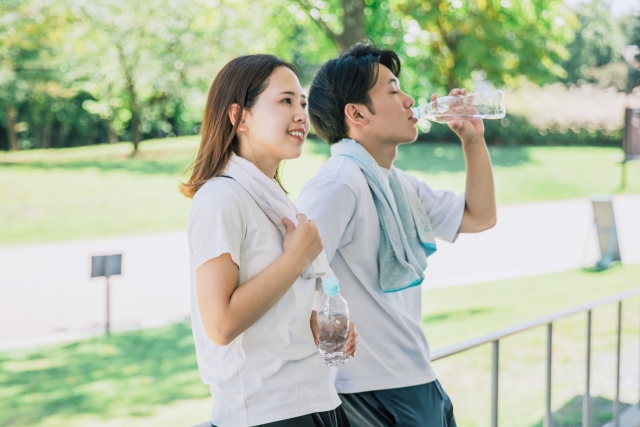 男女が汗を拭き、水分補給している姿